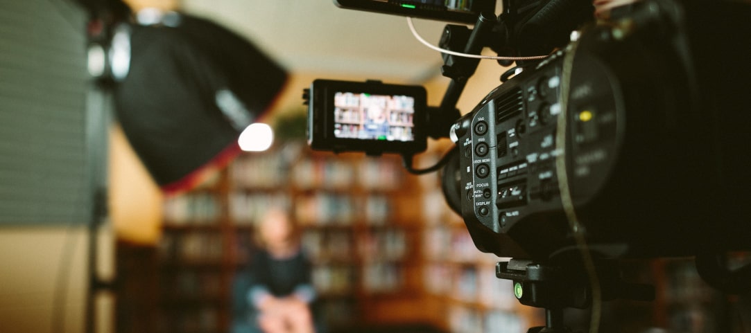 Video camera recording a person talking in front of a large bookcase